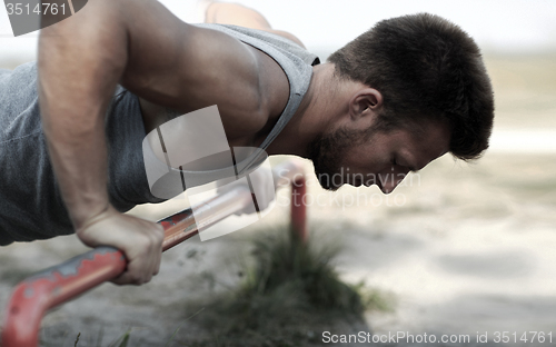 Image of young man exercising on horizontal bar outdoors