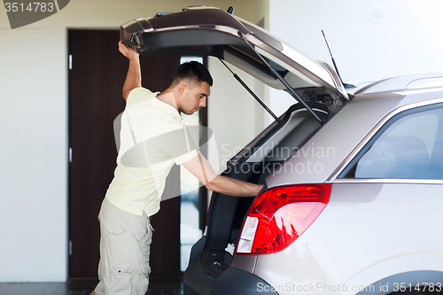 Image of young man with open car trunk at parking space