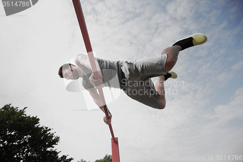 Image of young man exercising on horizontal bar outdoors