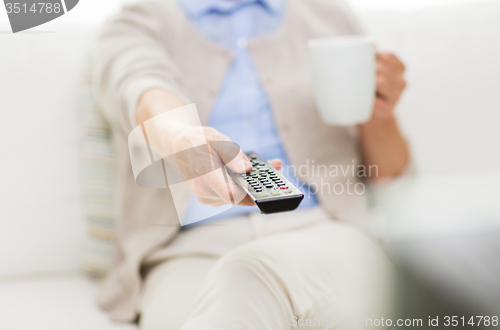 Image of senior woman watching tv and drinking tea at home