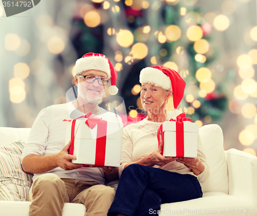 Image of happy senior couple in santa hats with gift boxes