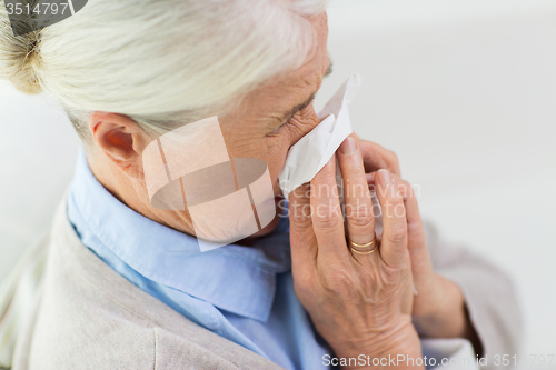 Image of sick senior woman blowing nose to paper napkin