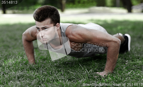 Image of young man doing push ups on grass in summer park