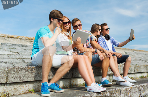 Image of group of smiling friends with tablet pc outdoors