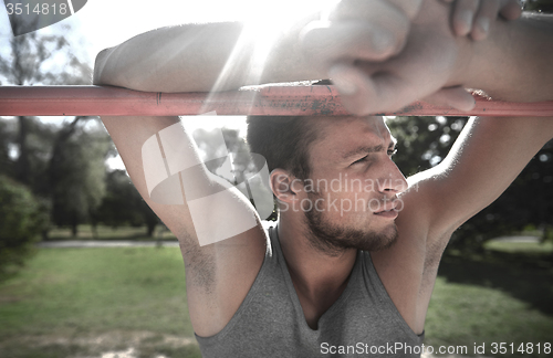 Image of young man exercising on horizontal bar outdoors