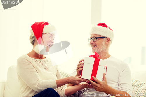 Image of happy senior couple in santa hats with gift box
