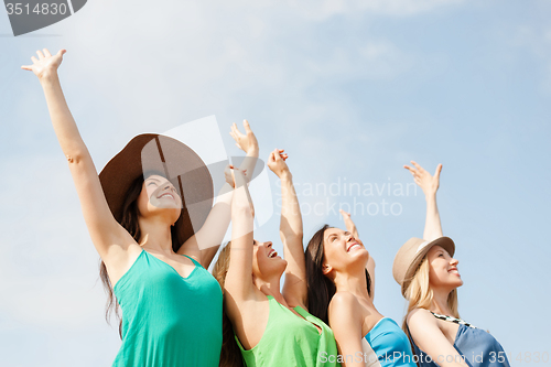 Image of smiling girls with hands up on the beach