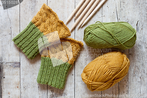 Image of wool green and yellow legwarmers, knitting needles and yarn 