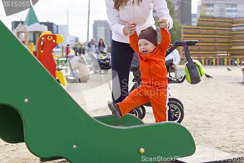 Image of One year boy on children's slide with mother