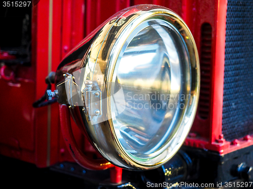Image of Closeup of brass headlight with glass on old red vehicle 