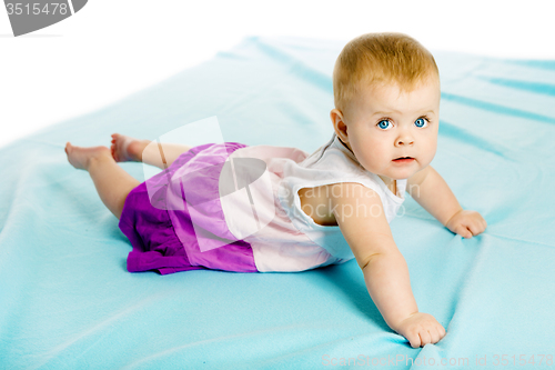 Image of baby girl in a dress creeps on the blue coverlet