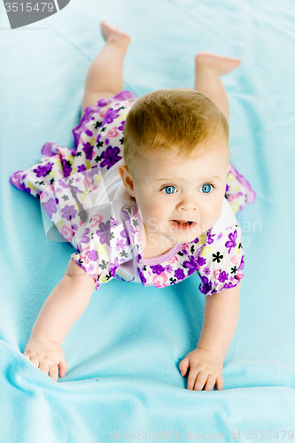 Image of baby girl in a dress creeps on the blue coverlet