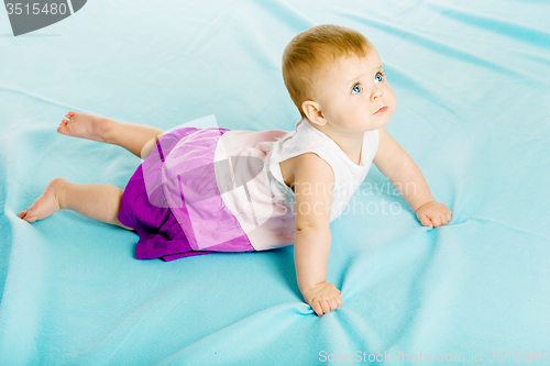 Image of baby girl in a dress creeps on the blue coverlet