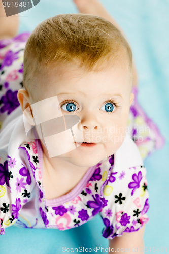 Image of baby girl in a dress creeps on the blue coverlet