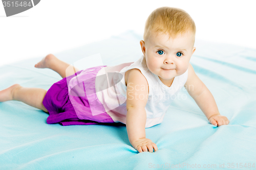 Image of baby girl in a dress creeps on the blue coverlet