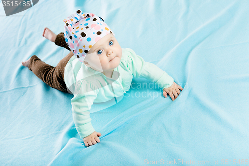 Image of baby in hat crawling on the blue coverlet