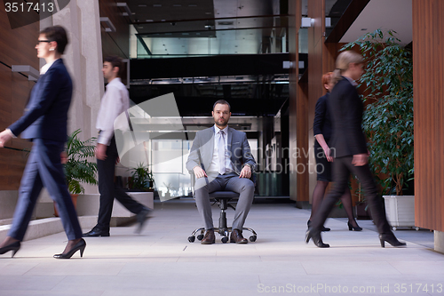 Image of business man sitting in office chair, people group  passing by