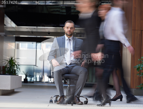 Image of business man sitting in office chair, people group  passing by