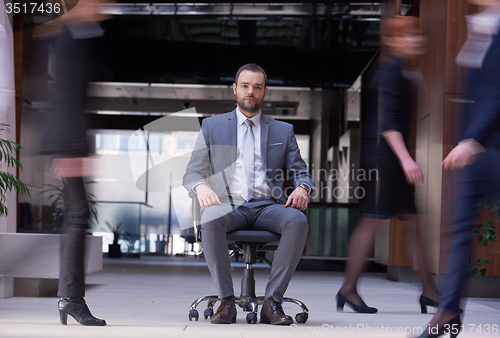 Image of business man sitting in office chair, people group  passing by