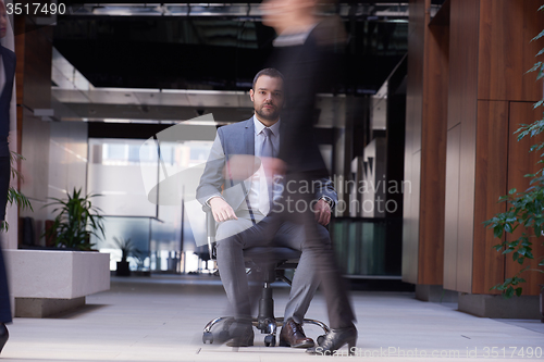 Image of business man sitting in office chair, people group  passing by