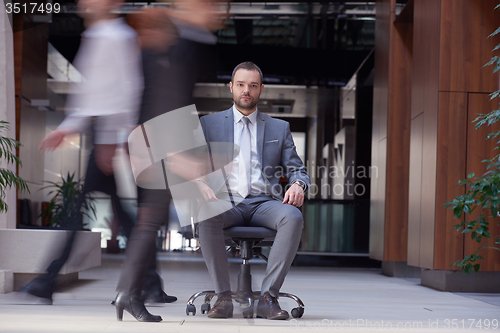 Image of business man sitting in office chair, people group  passing by