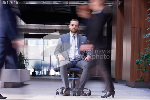 Image of business man sitting in office chair, people group  passing by