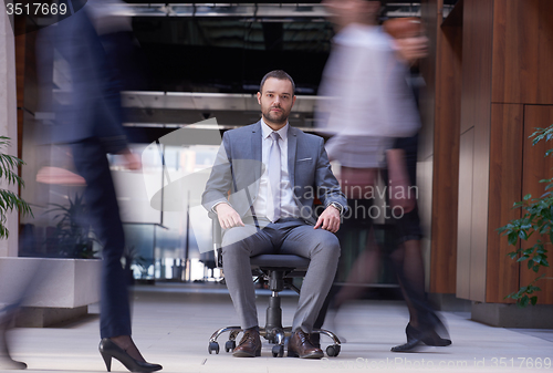 Image of business man sitting in office chair, people group  passing by