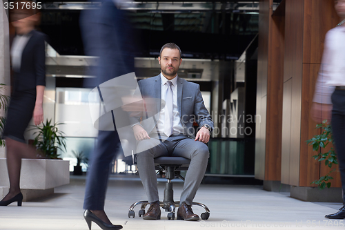 Image of business man sitting in office chair, people group  passing by