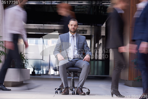 Image of business man sitting in office chair, people group  passing by