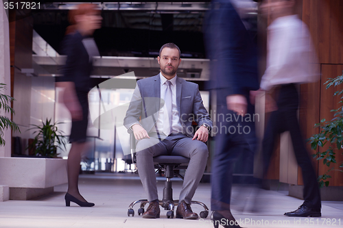 Image of business man sitting in office chair, people group  passing by