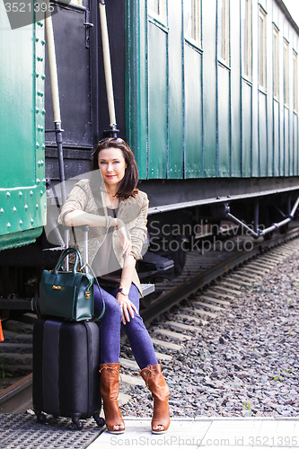 Image of woman with a suitcase and handbag sitting on the steps of the pa