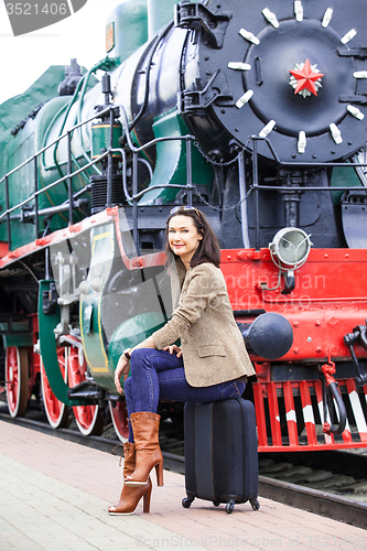 Image of smiling beautiful middle-aged woman sitting on a suitcase