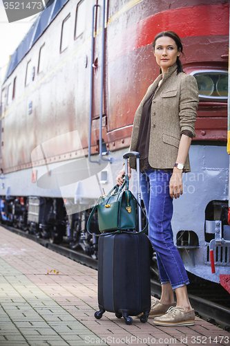 Image of beautiful middle-aged woman with luggage near retro train