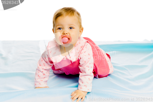 Image of baby girl with pacifier crawling on the blue coverlet. Studio