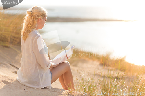 Image of Woman enjoys reading on beautiful sandy beach.