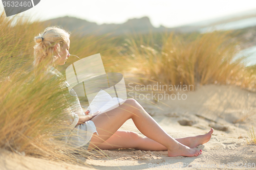 Image of Woman enjoys reading on beautiful sandy beach.