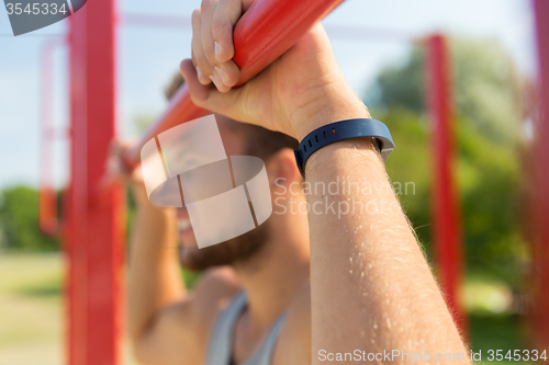 Image of young man exercising on horizontal bar outdoors