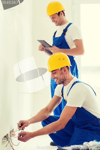 Image of builders with tablet pc and fixing wiring indoors