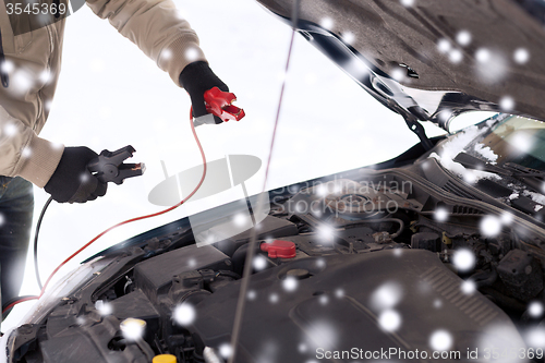 Image of closeup of man under bonnet with starter cables