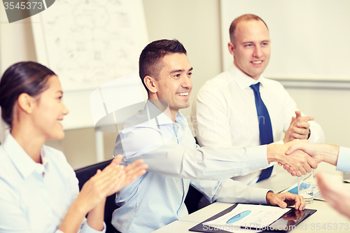 Image of smiling business team shaking hands in office