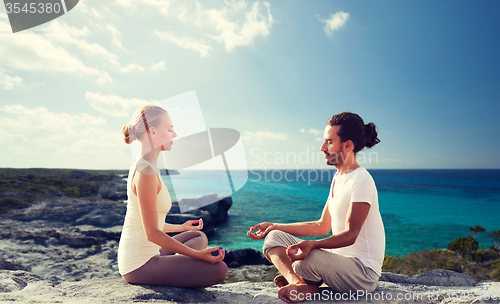 Image of happy couple meditating in lotus pose on beach