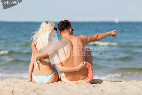 Image of happy couple in swimwear sitting on summer beach