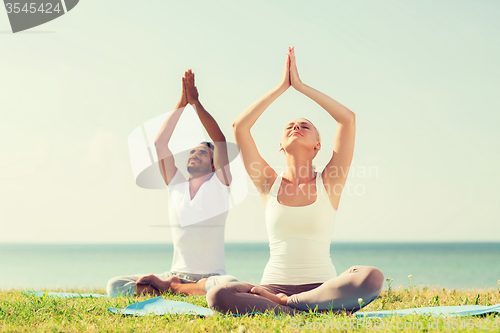 Image of smiling couple making yoga exercises outdoors