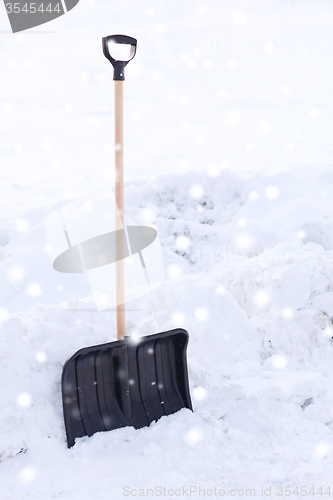 Image of black snowshowel with wooden handle in snow pile