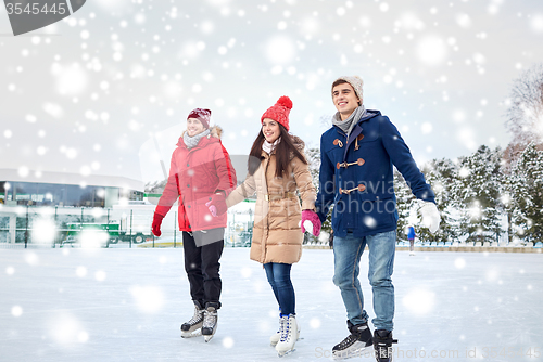 Image of happy friends ice skating on rink outdoors