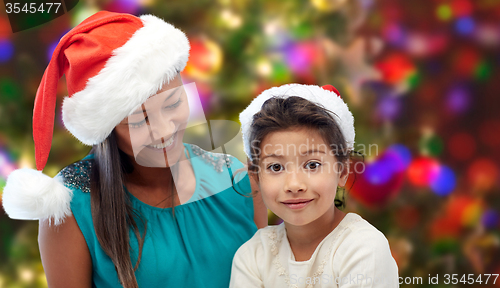 Image of happy mother and little girl in santa hats at home