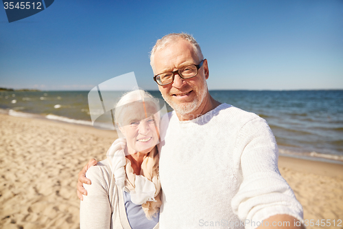 Image of seniors taking picture with selfie stick on beach