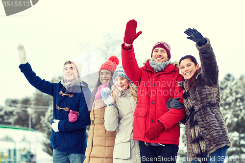 Image of happy friends waving hands on ice rink outdoors