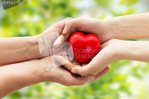 Image of senior and young woman hands holding red heart
