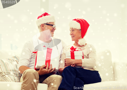 Image of happy senior couple in santa hats with gift boxes